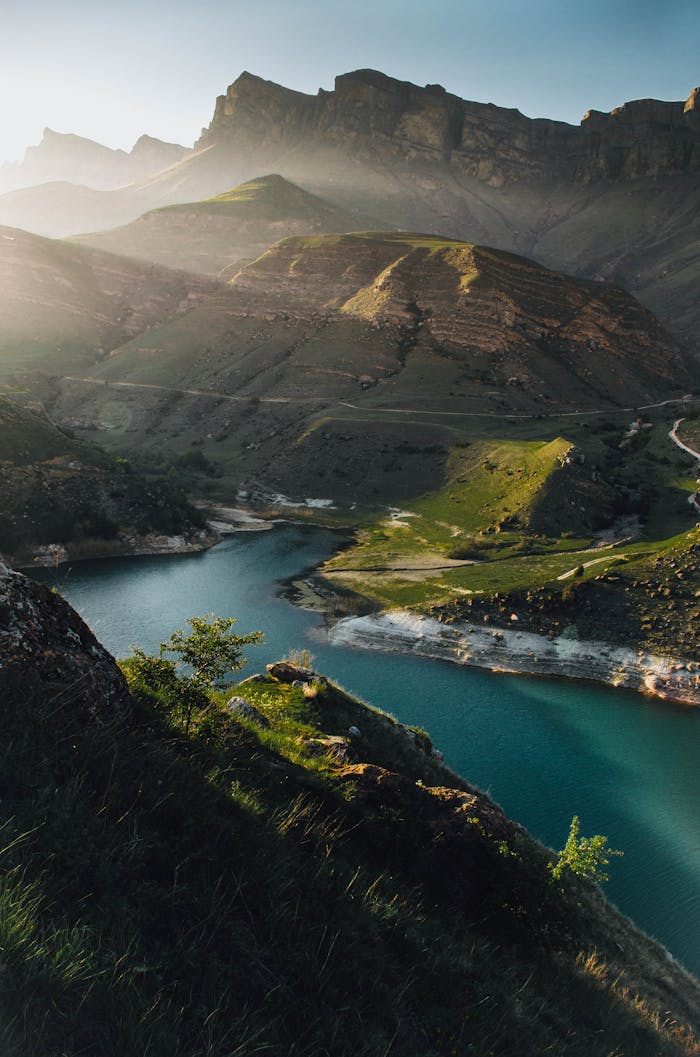 Capture of a serene mountain valley with a winding river and lush scenery at sunset.